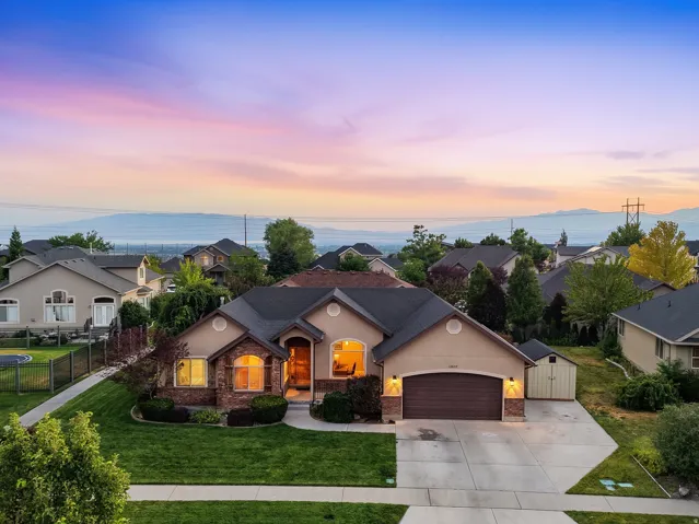Stunning single-story residence showcasing a warm stucco exterior with arched entryways, professionally landscaped grounds featuring mature trees and manicured lawn, a three-car attached garage with dark finish, and abundant windows flooding the interior