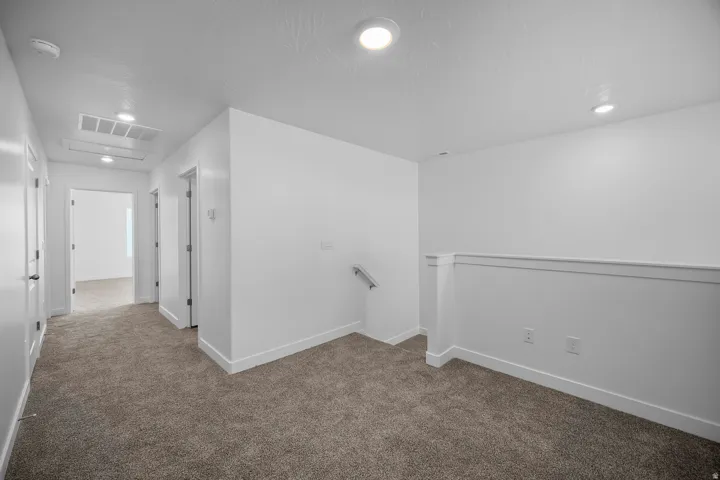 Carpeted hallway with white walls and trim, recessed lighting, and a white interior railing