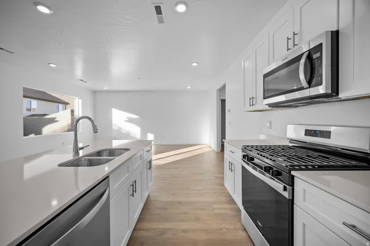 Kitchen featuring white cabinetry, light-toned countertops, stainless steel appliances, and wood-finish flooring