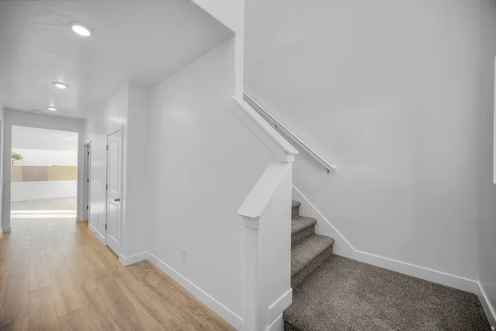 Wood-finish flooring, recessed ceiling lighting, white painted walls, white trim, and a carpeted staircase with a white handrail