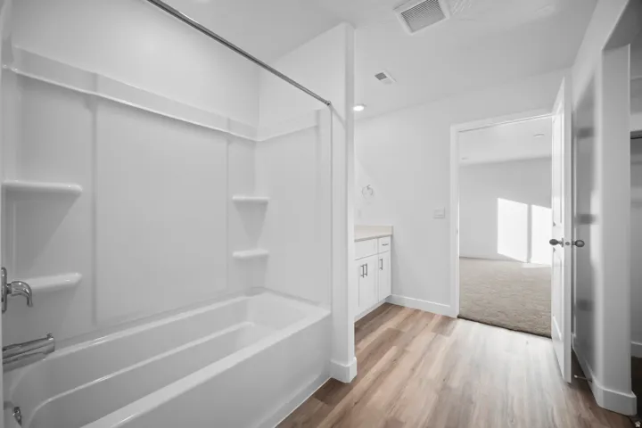 Full bathroom featuring a white tub/shower combination, white vanity with a light-toned countertop, and wood-finish flooring