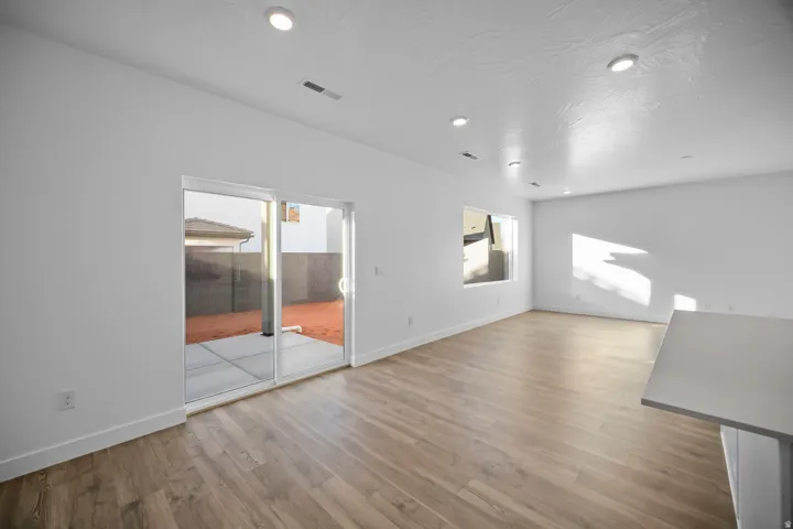 Wood-finish flooring, recessed ceiling lighting, and a sliding glass door leading to a concrete patio