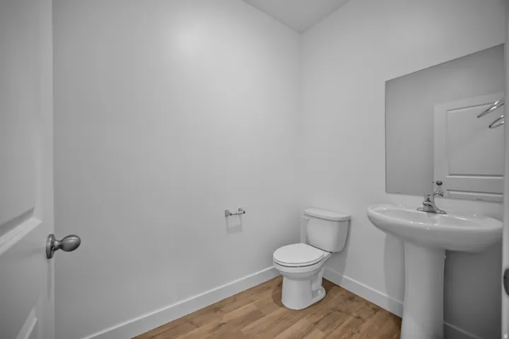 White walls, pedestal sink, wall-mounted mirror, two-piece toilet, wood-finish flooring