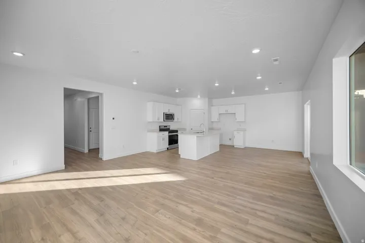 Open-concept living space with wood-finish flooring, recessed lighting, and a kitchen featuring white cabinetry, light countertops, and stainless steel appliances