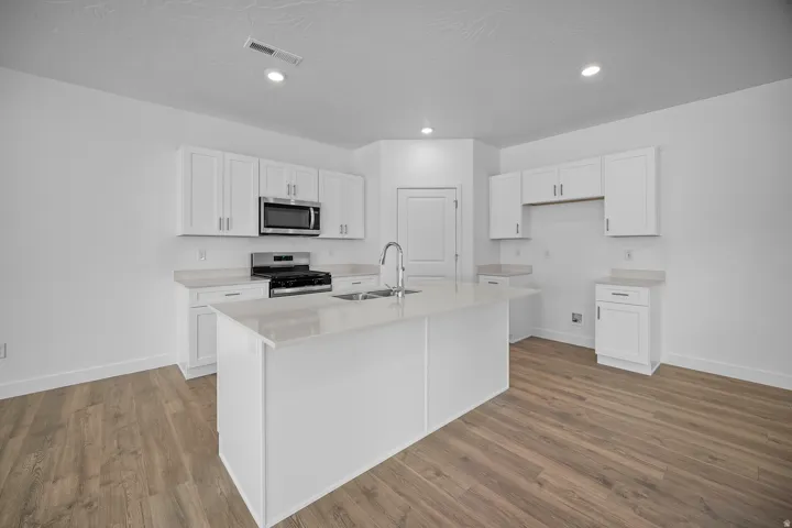 Kitchen featuring wood-finish flooring, white cabinetry, a center island with sink, stainless steel appliances, and recessed lighting