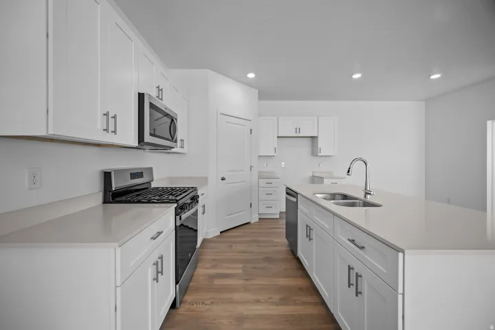 White cabinetry with brushed nickel hardware, stainless steel appliances, light-toned countertops, wood-finish flooring, and recessed lighting