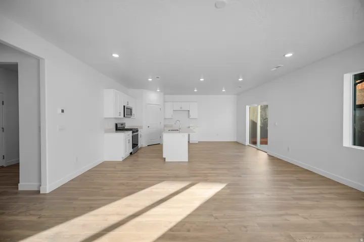 Open-concept living area featuring wood-finish flooring, recessed lighting, and a kitchen with white cabinetry and an island