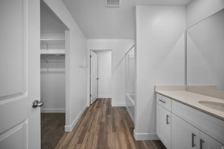 Wood-finish flooring, white shaker-style vanity with a light-toned countertop, and an integrated tub-shower combination