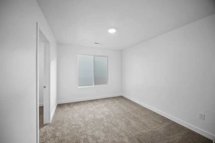 Recessed lighting illuminates the room, featuring a neutral carpet and a window with frosted glass