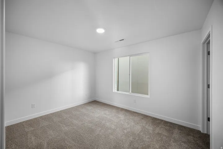 Recessed ceiling lighting, a sliding window, light-colored walls, and gray-toned carpeting