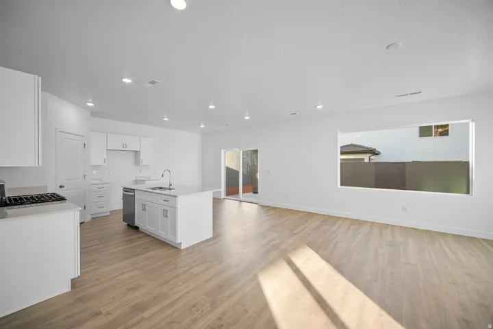 Open-concept living area featuring wood-finish flooring, recessed lighting, a kitchen island with a sink, white cabinetry, and a gas range