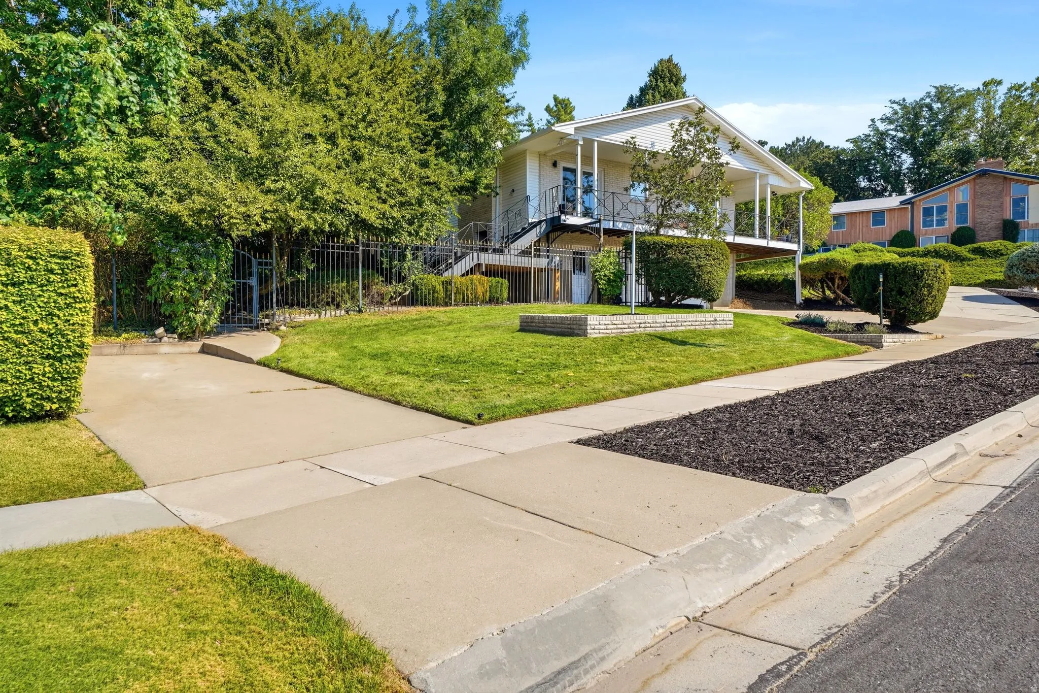 Spacious front yard featuring a manicured lawn, established landscaping, and a concrete driveway