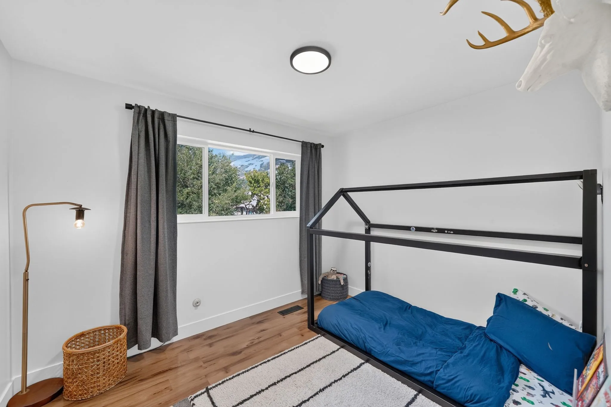 Bright secondary bedroom featuring a black metal canopy bed frame, wood-finish flooring, and large picture window with natural light