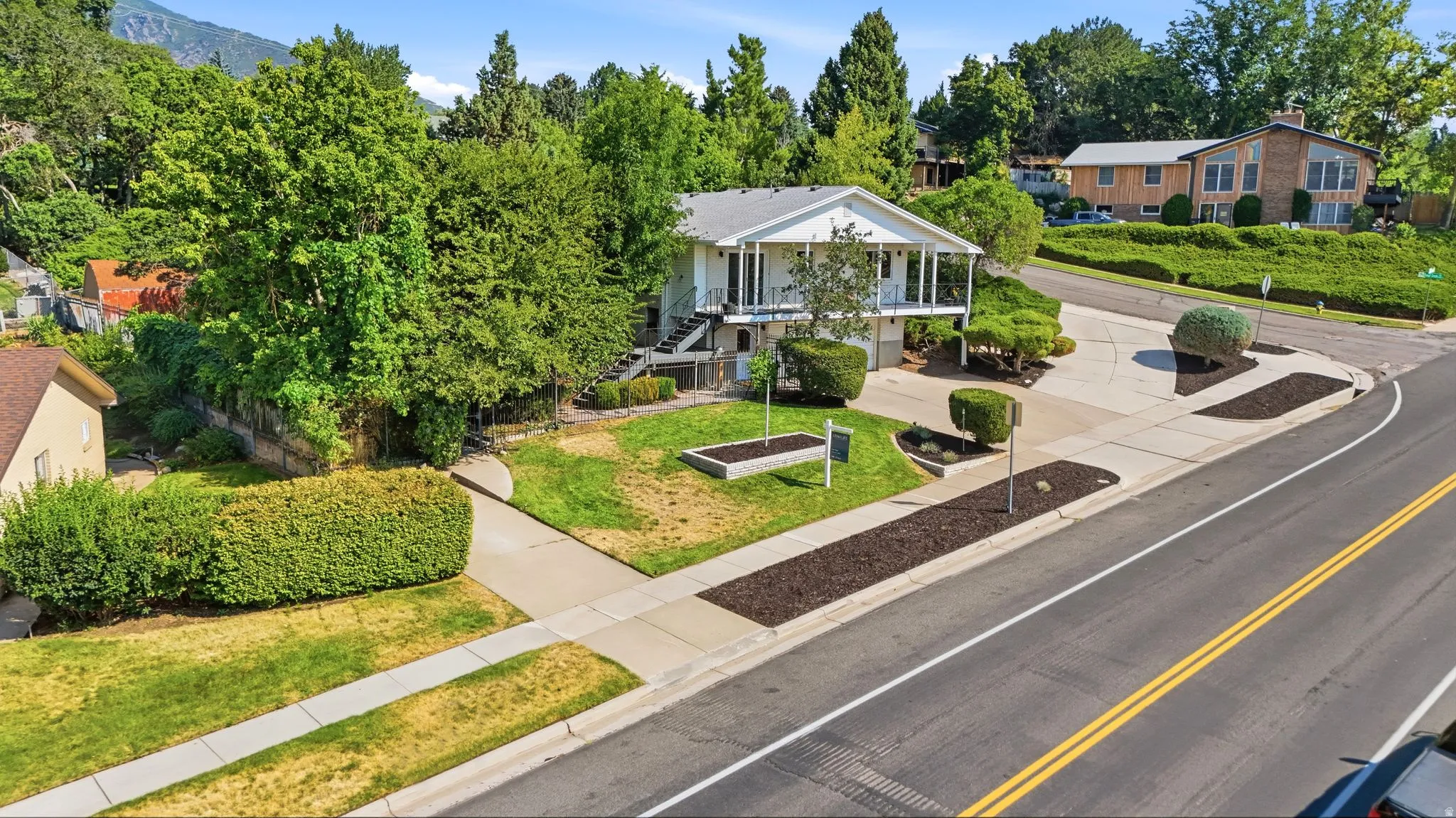 Two-story residence with a covered upper-level balcony, paved driveway, and established landscaping