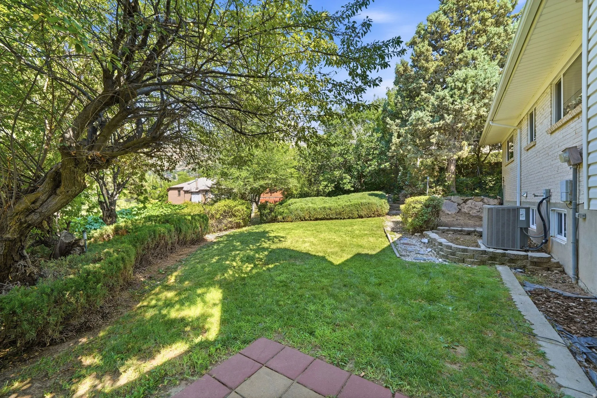 Expansive backyard oasis featuring a meticulously manicured lawn, mature shade trees providing natural canopy coverage, and established landscaping with hedges and garden beds