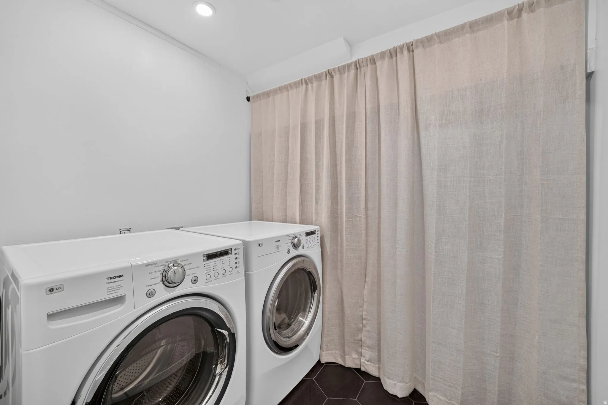 Recessed ceiling lighting, dark hexagonal floor tiling, and a floor-to-ceiling curtain