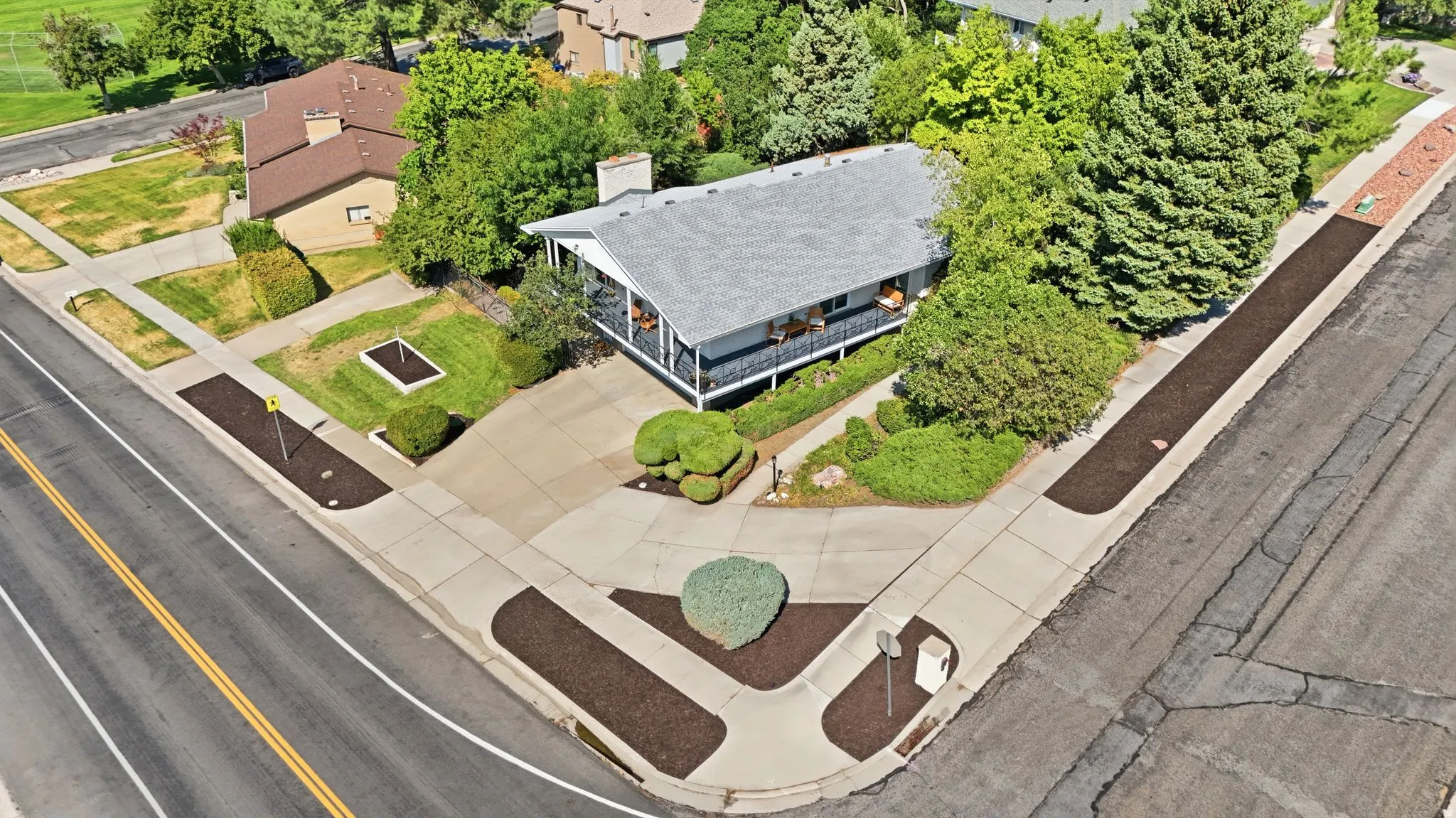 Corner lot residence featuring mature landscaping, a paved driveway, and a front porch with railing