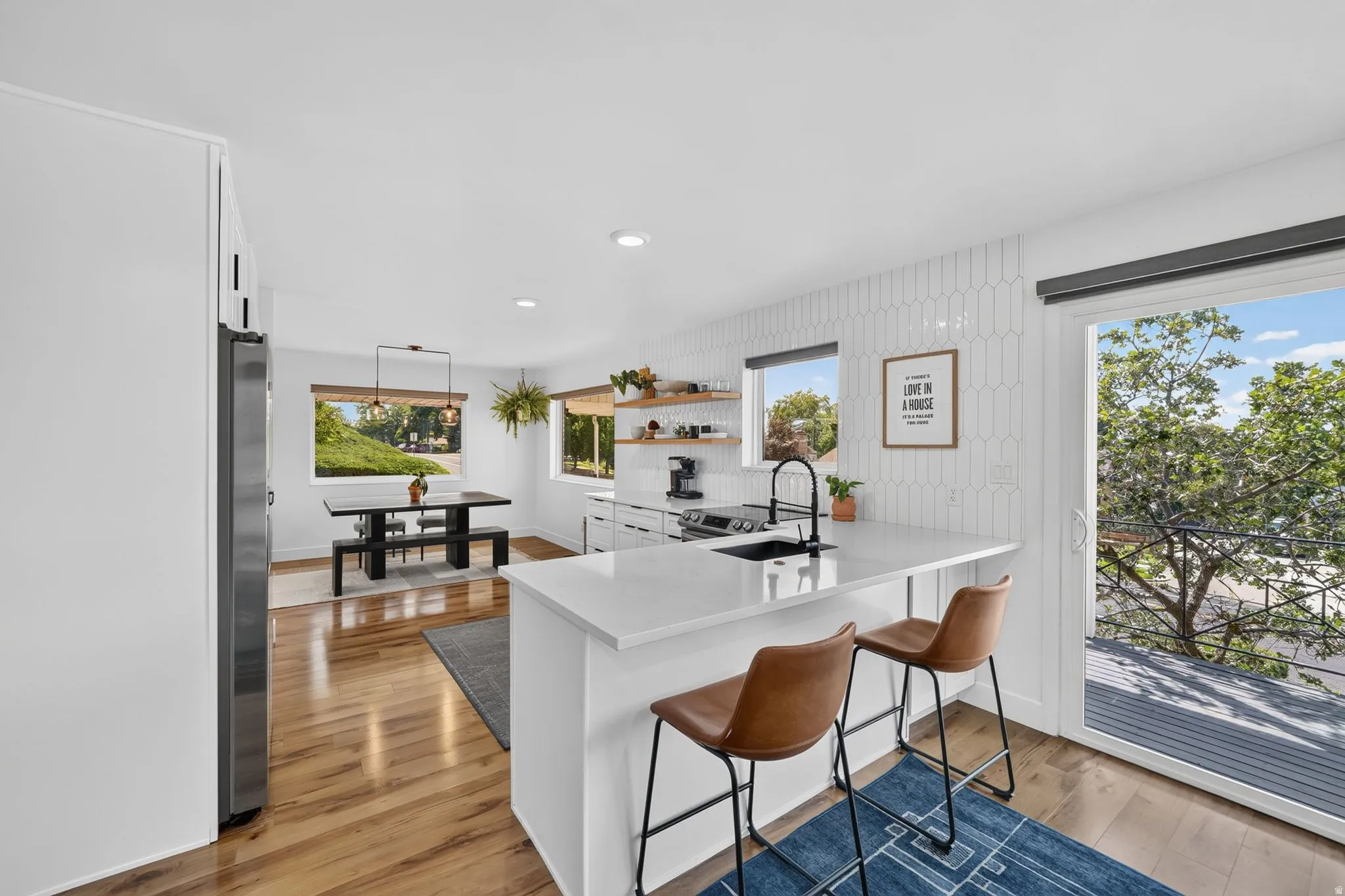 Modern kitchen featuring a white waterfall-edge island with seating for two, stainless steel appliances including a professional-style range, white cabinetry with integrated hardware, wood-finish flooring, and expansive sliding glass doors opening to outd