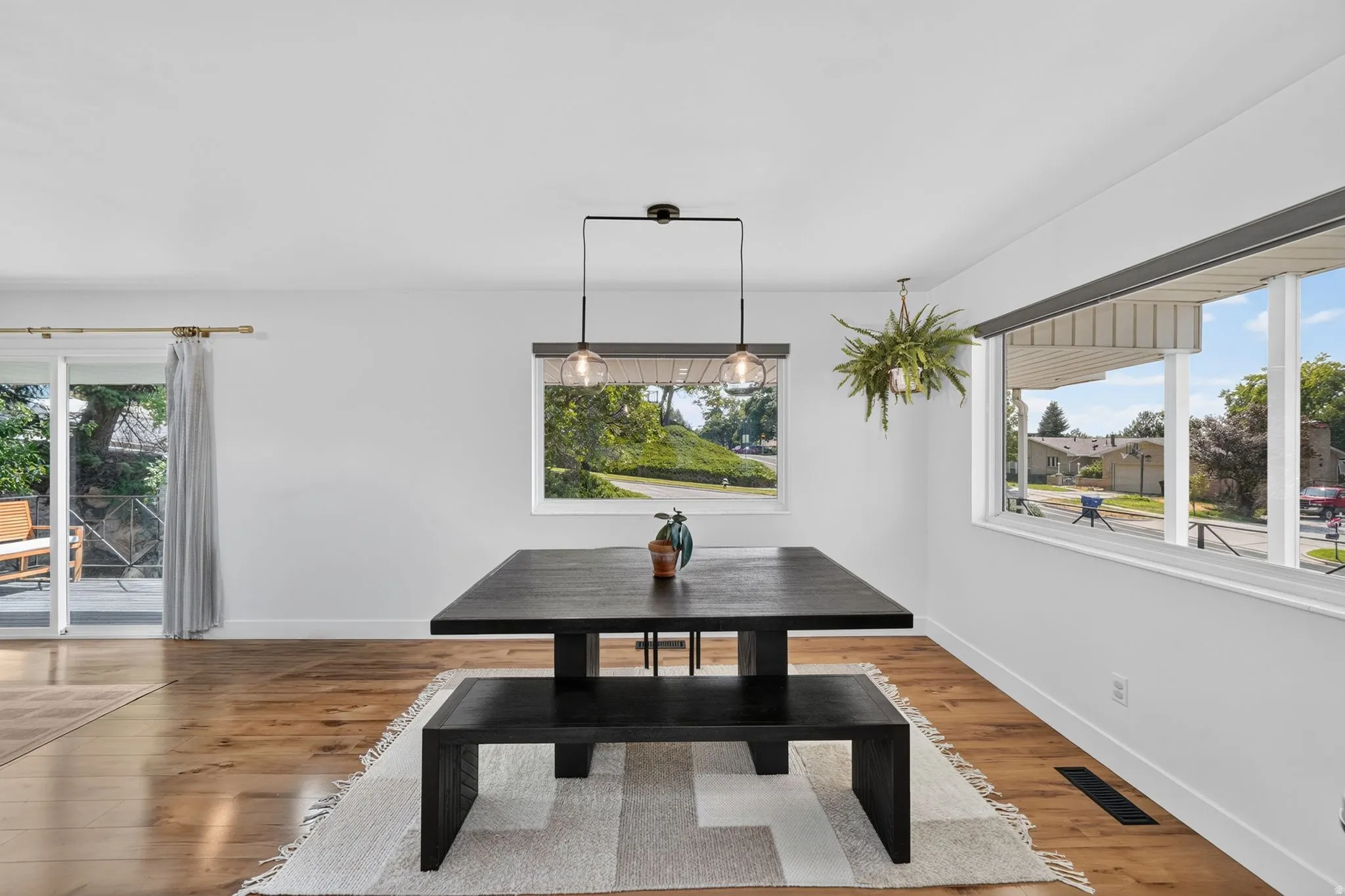 Dining room showcasing hardwood flooring, a black rectangular dining table with bench seating, and abundant natural light from multiple windows