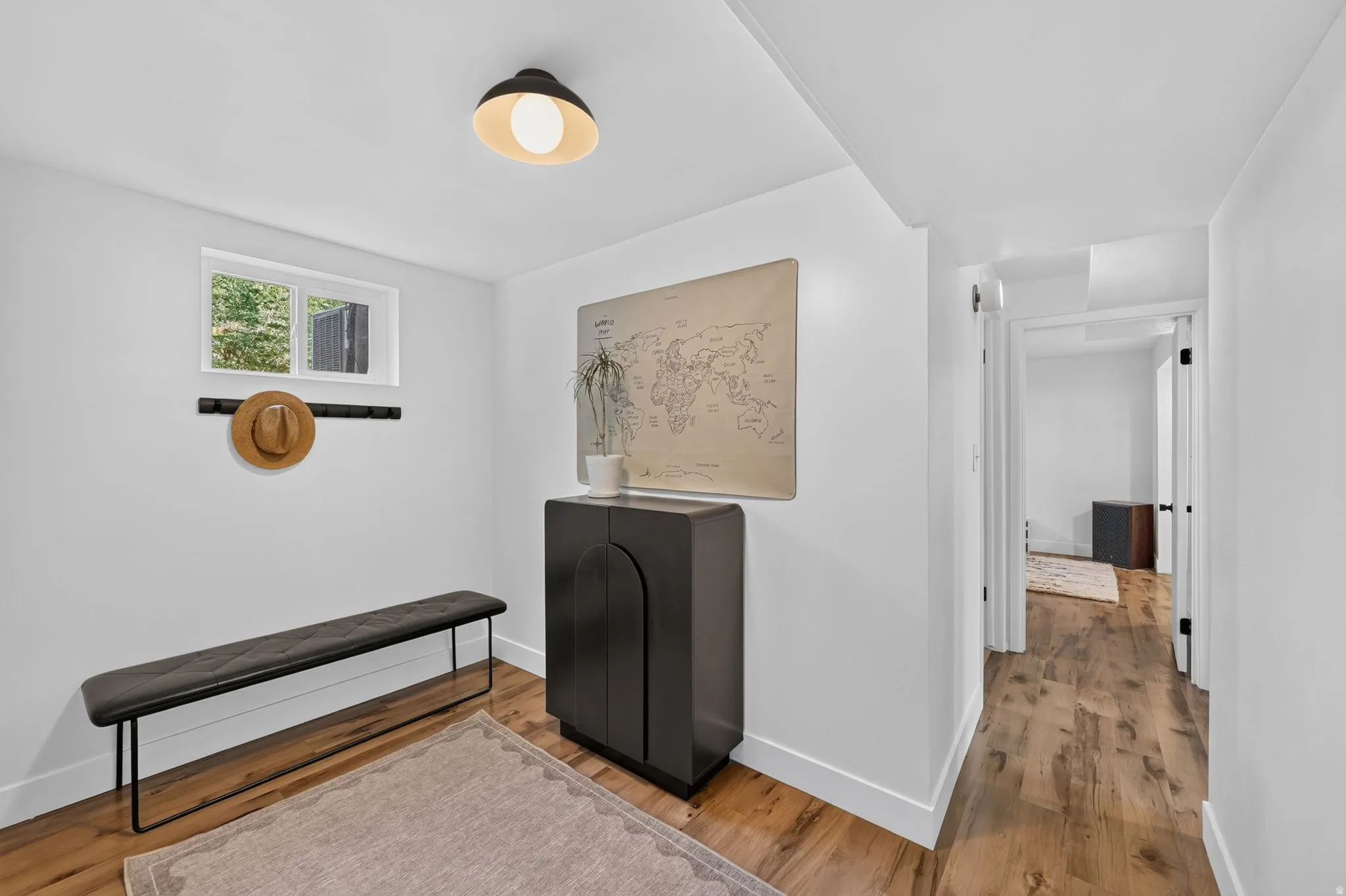 White walls with wood-finish flooring, a contemporary black ceiling light fixture, and a built-in wall-mounted coat rack