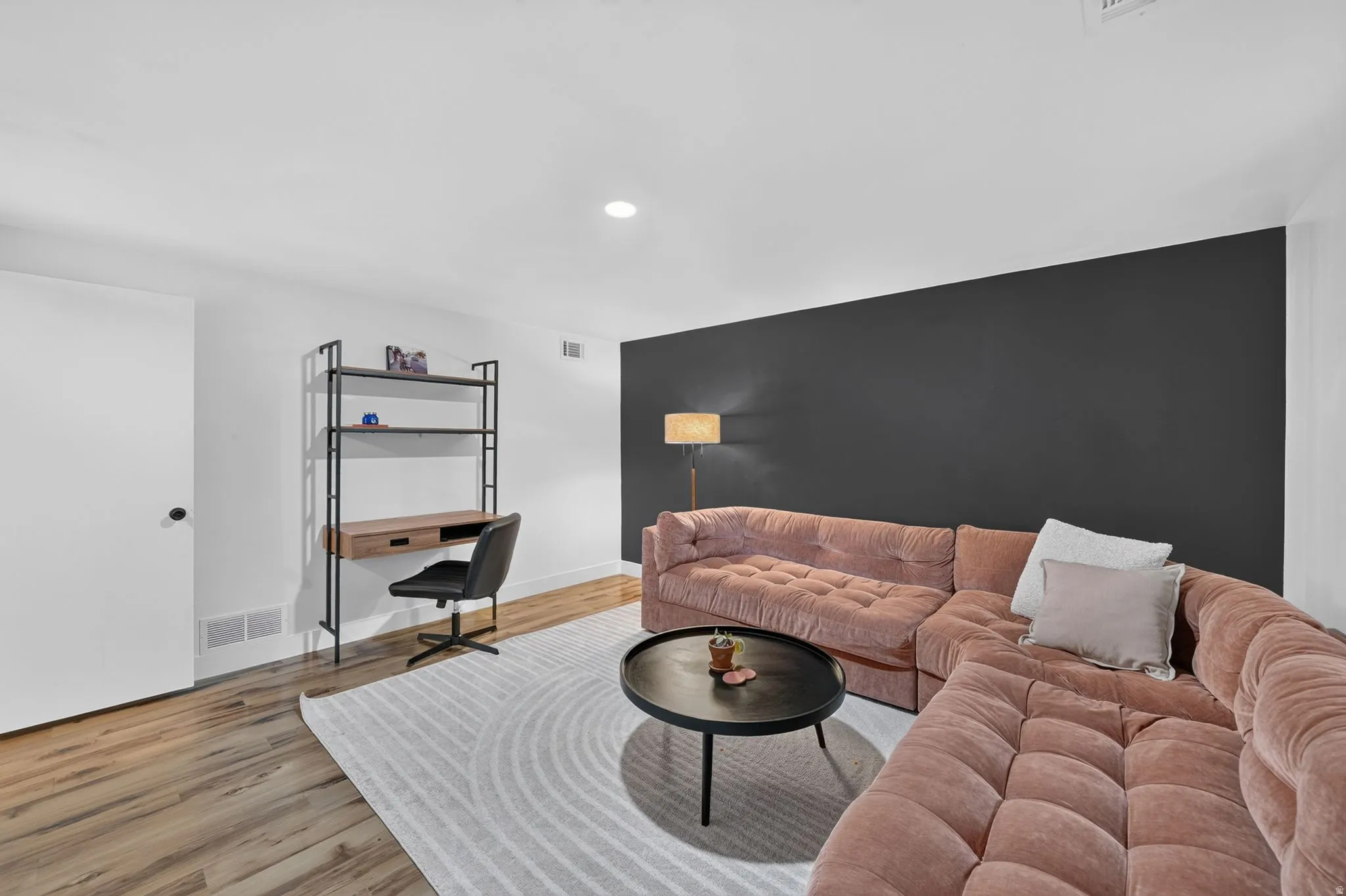 Modern living space featuring a taupe quilted sectional sofa, wood-finish flooring throughout, and a striking charcoal accent wall