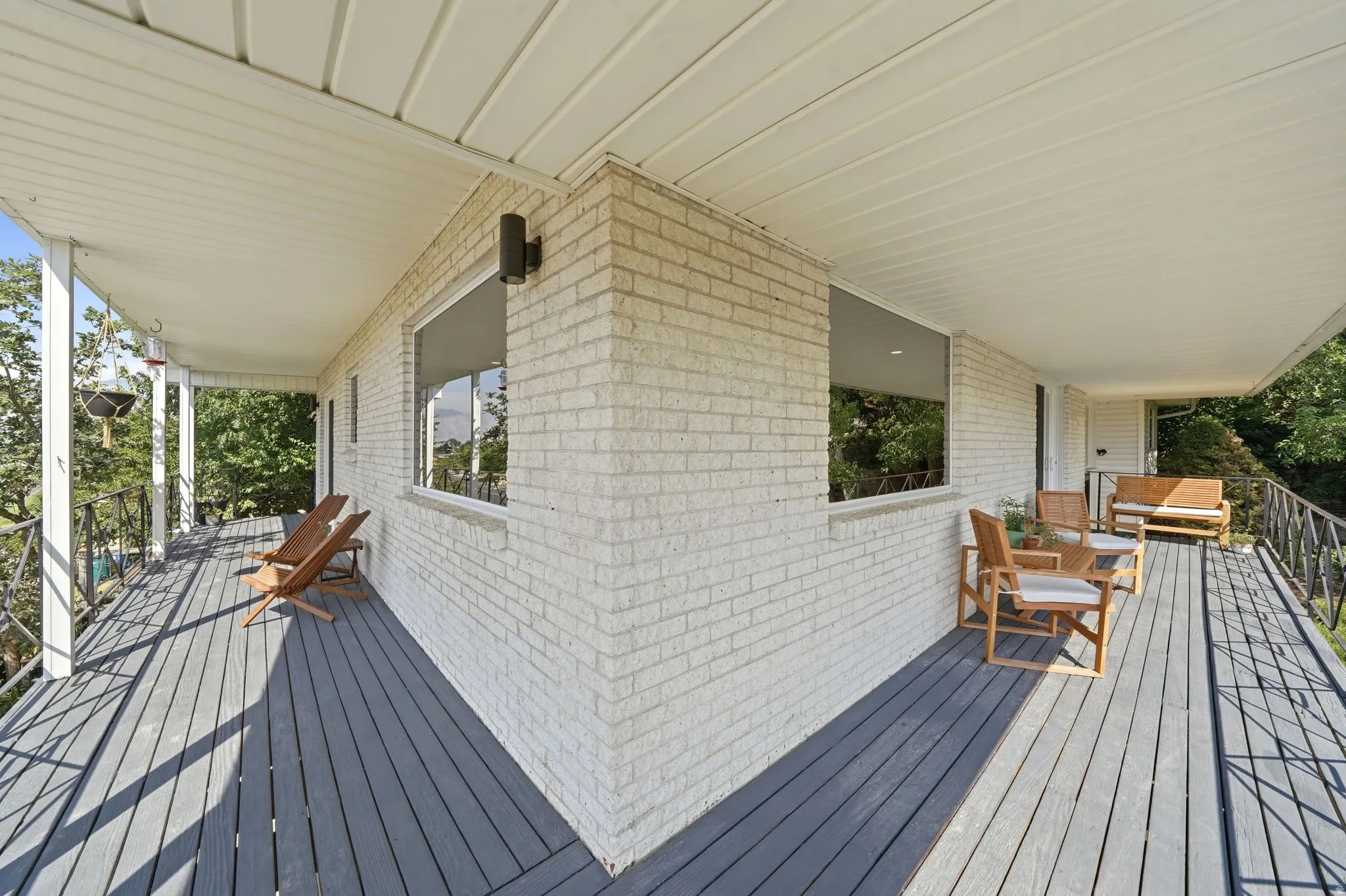 Expansive wraparound deck with composite decking and multiple covered pavilion sections, anchoring a modern white brick structure with large multi-pane windows and clean architectural lines