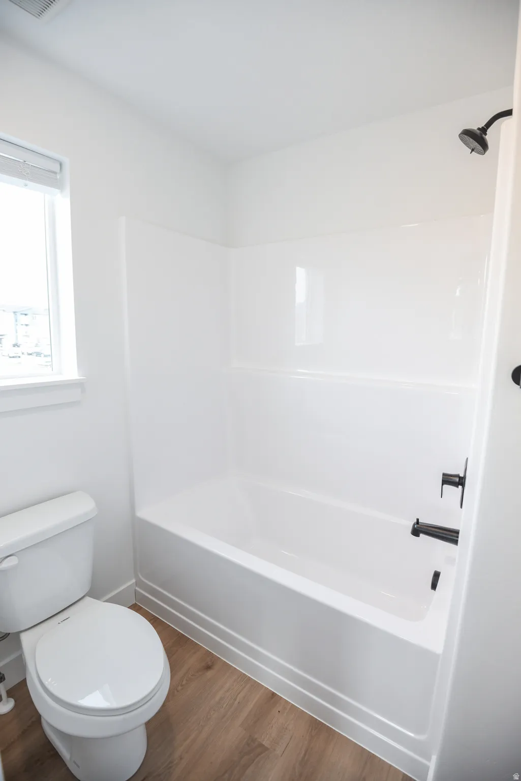 White bathtub with matte black fixtures, white toilet, and wood-finish flooring