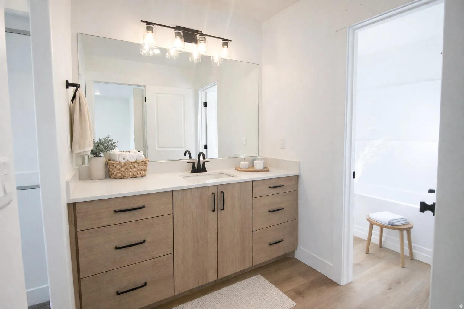 Double vanity with light wood-finish cabinetry, black hardware, and an integrated sink