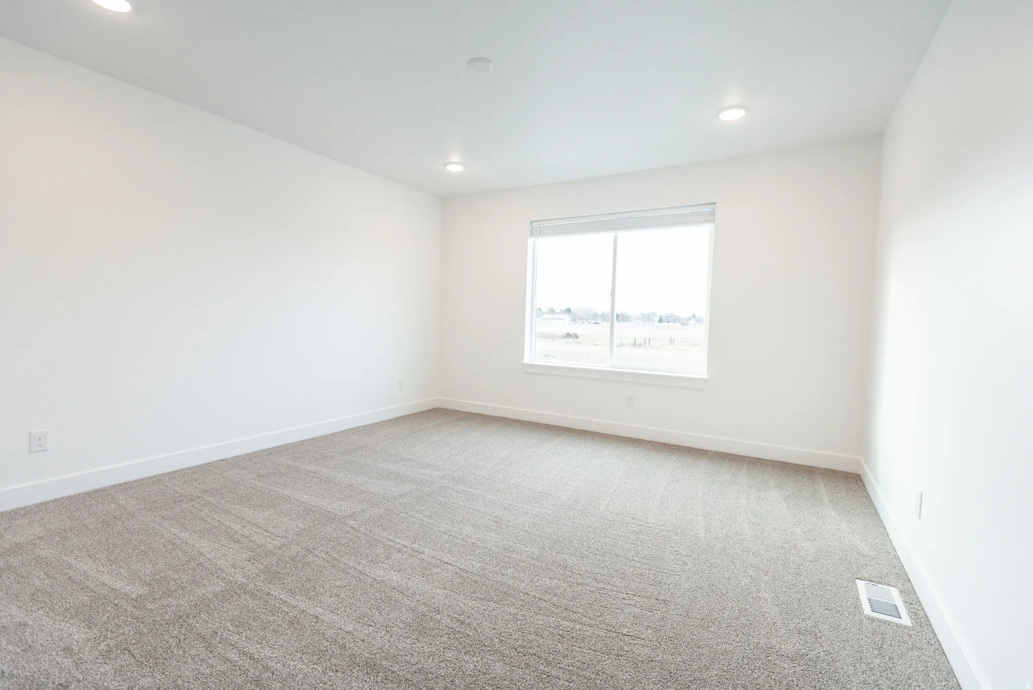 Recessed lighting, wall-to-wall carpeting, and a large window with roller shades