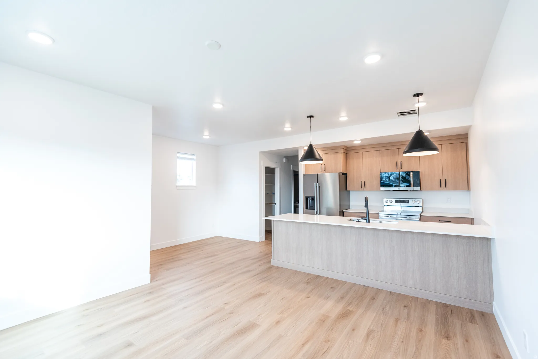 Open-concept living space featuring wood-finish flooring, recessed lighting, and a kitchen island with pendant lights