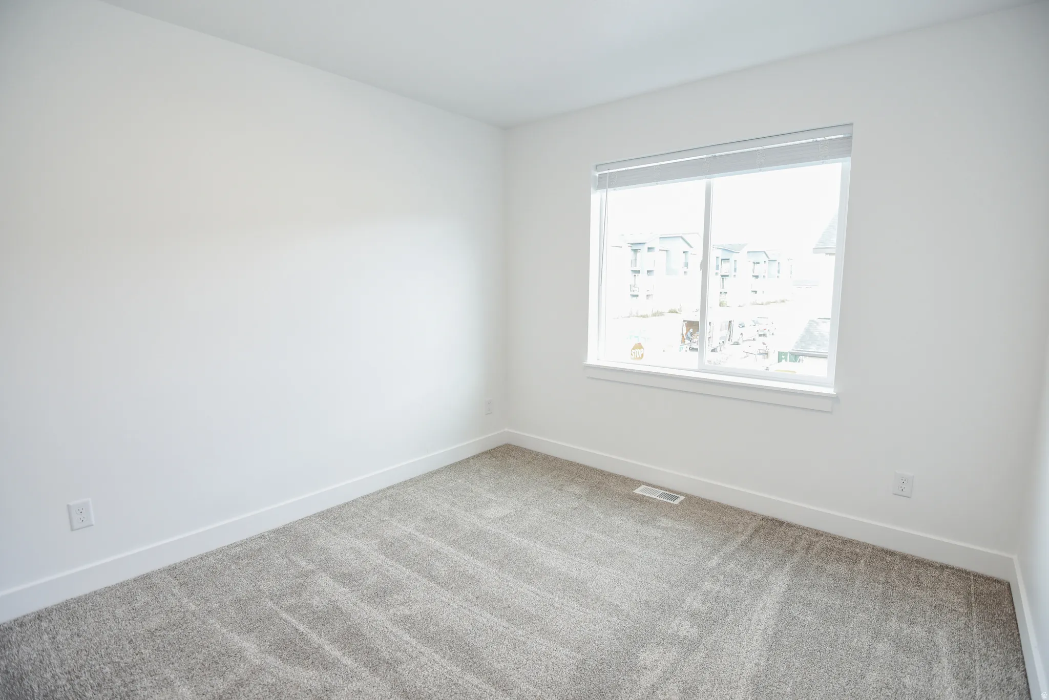 White painted walls, grey carpeting, and a window with white blinds