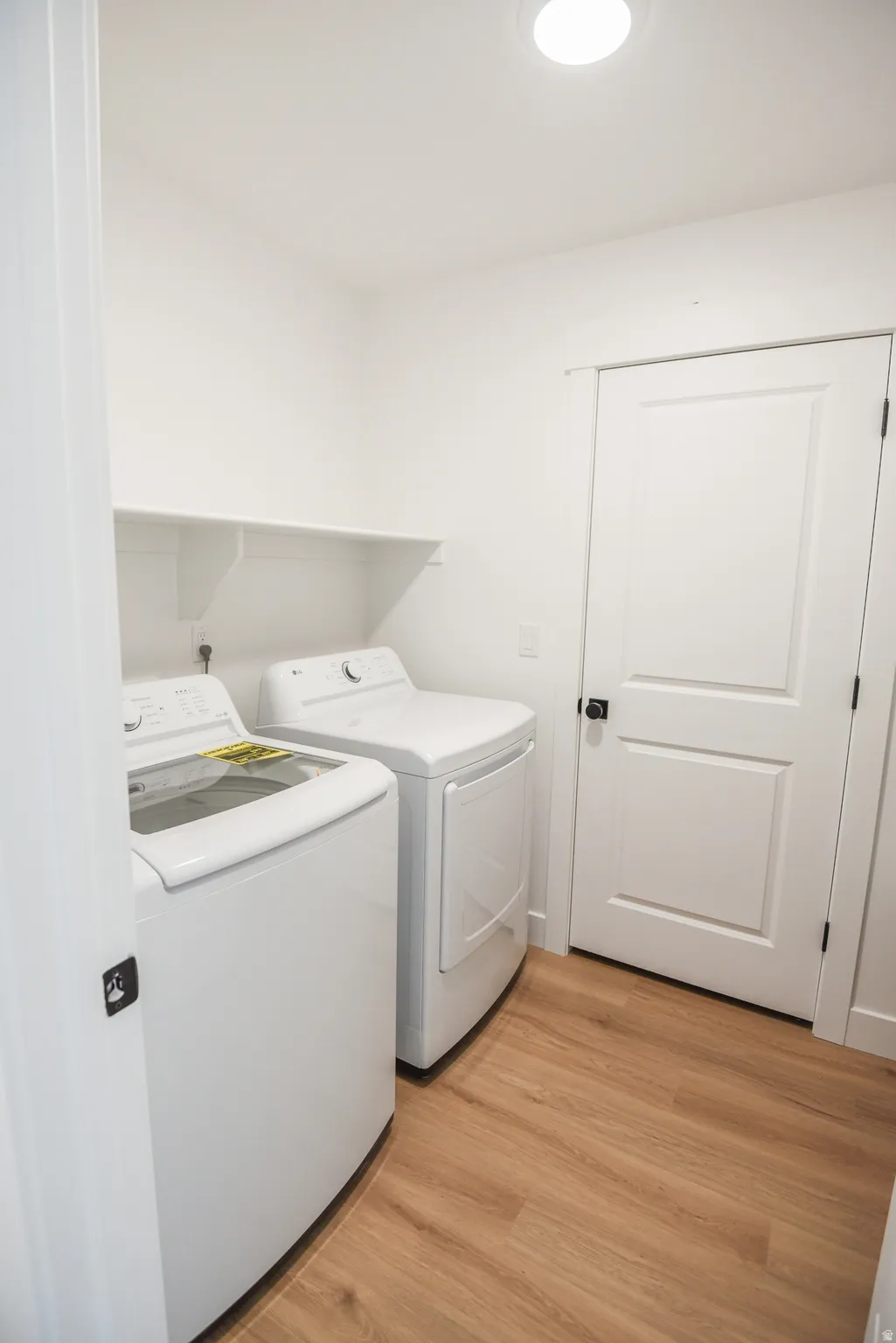 Laundry space featuring wood-finish flooring, white walls, and a built-in white shelf