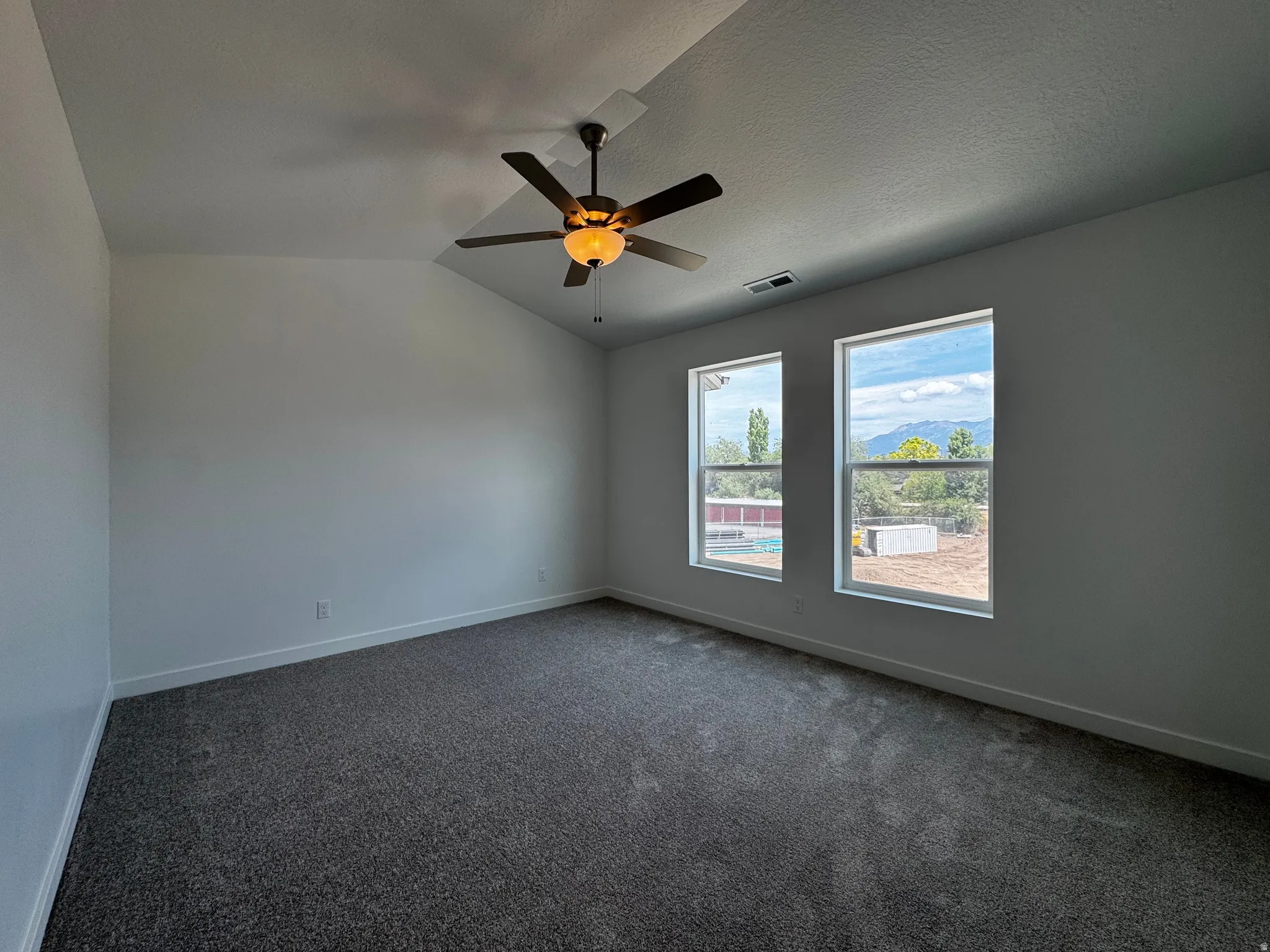 Vaulted ceiling with an integrated ceiling fan, two windows with mountain scenery, and dark gray carpet