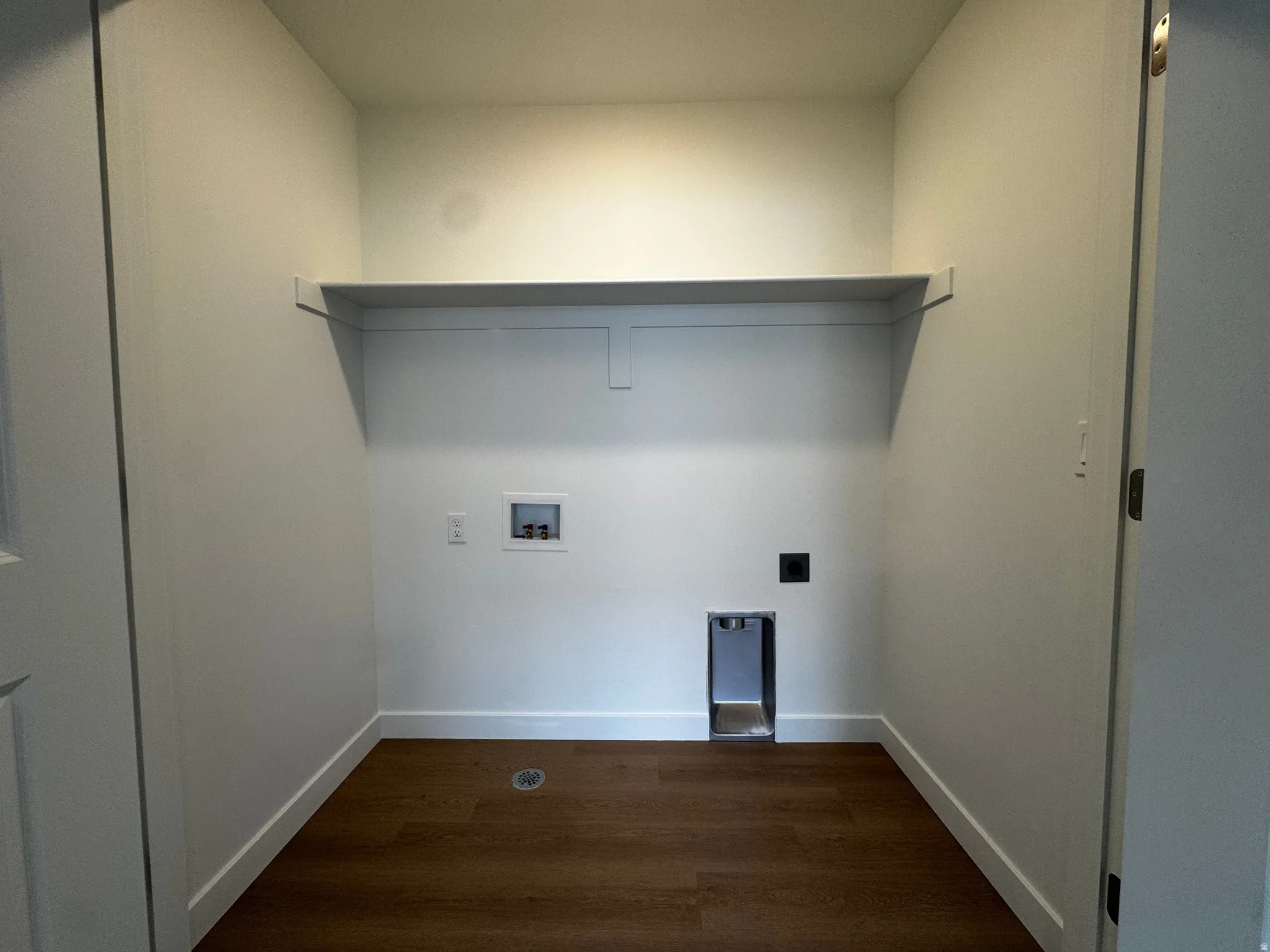 Dedicated laundry area with a built-in shelf and wood-finish flooring
