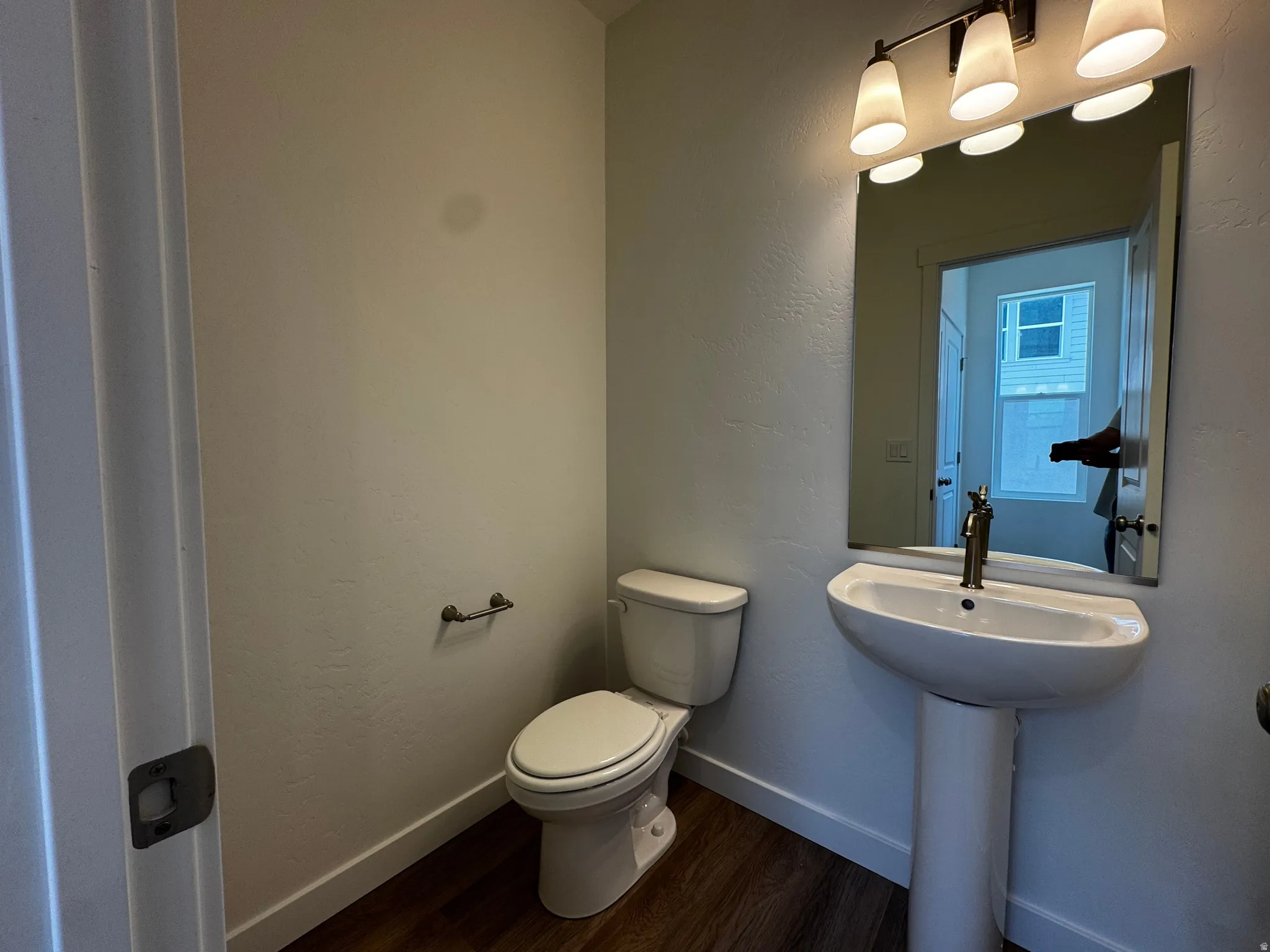 Pedestal sink with a polished brass faucet, rectangular mirror, and a three-light vanity fixture