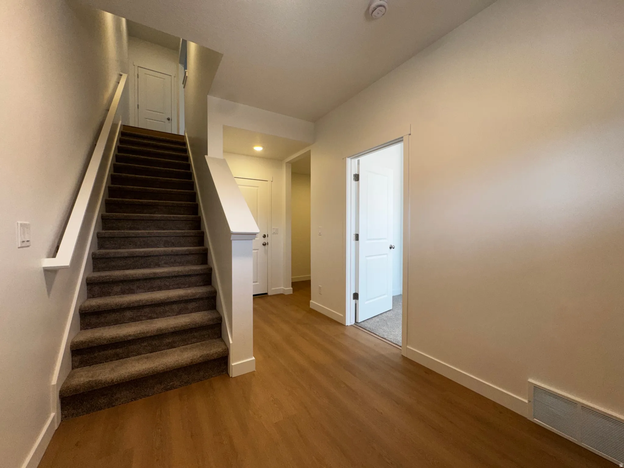 Wood-finish flooring, carpeted staircase, white interior doors, and recessed lighting