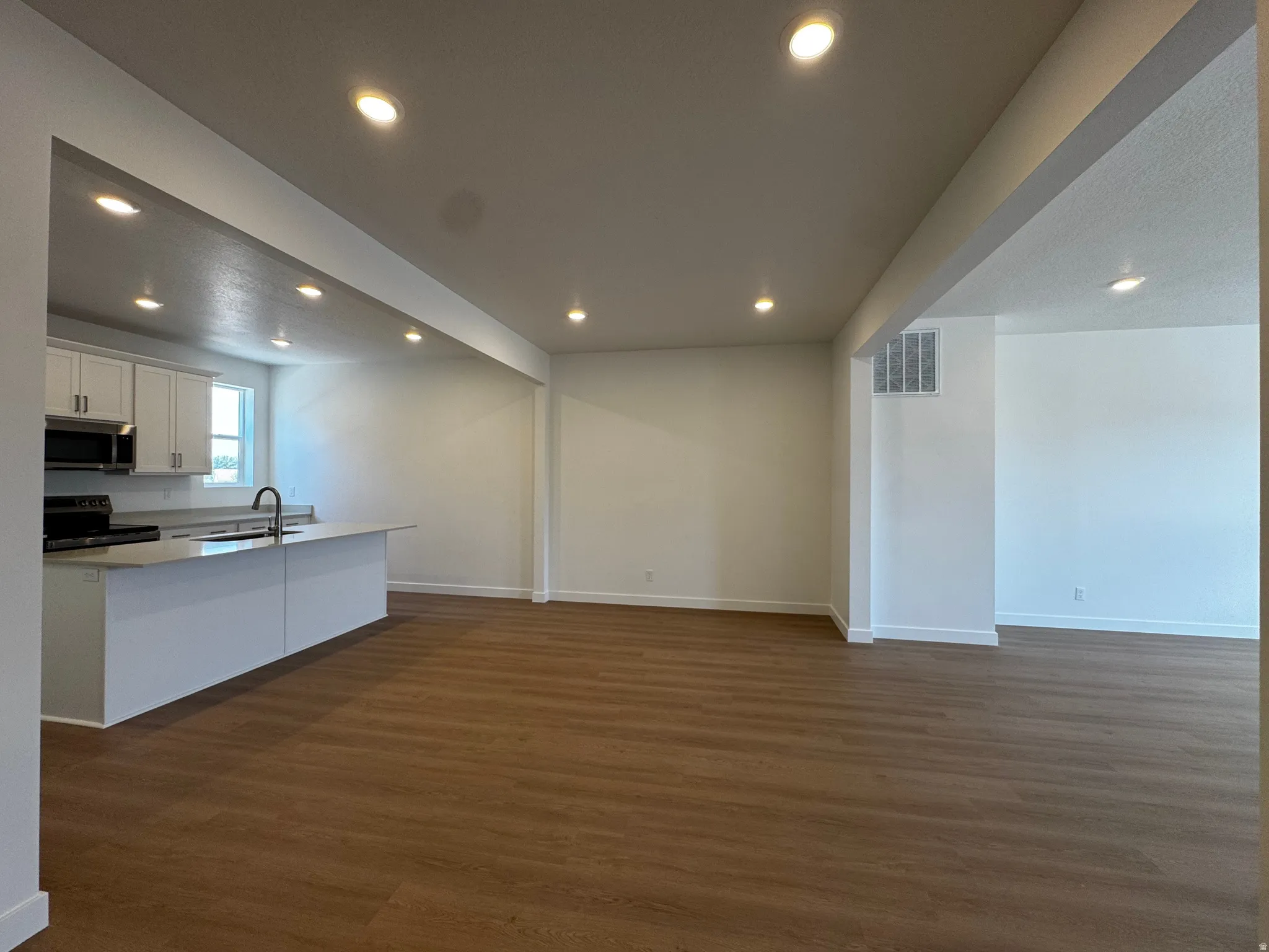Open-concept living space with wood-finish flooring, recessed lighting, and a kitchen island with a sink