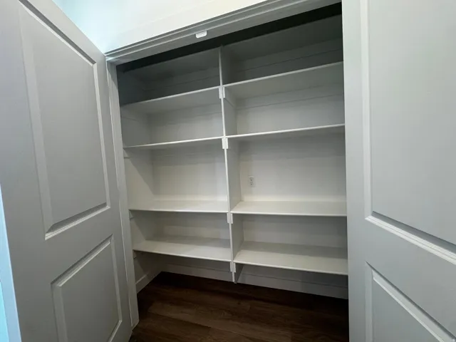 Recessed shelving with multiple fixed shelves, wood-finish flooring, and white paneled doors