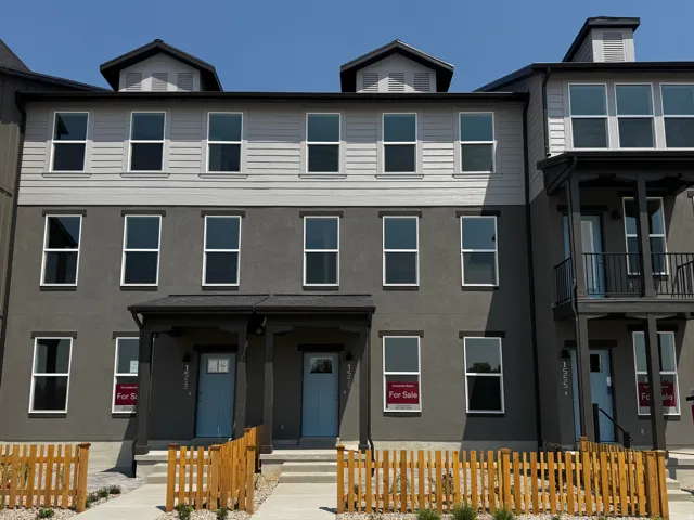 Multi-story townhome with a stucco and siding exterior, multiple windows, front porches with light blue doors, and individual fenced front yards