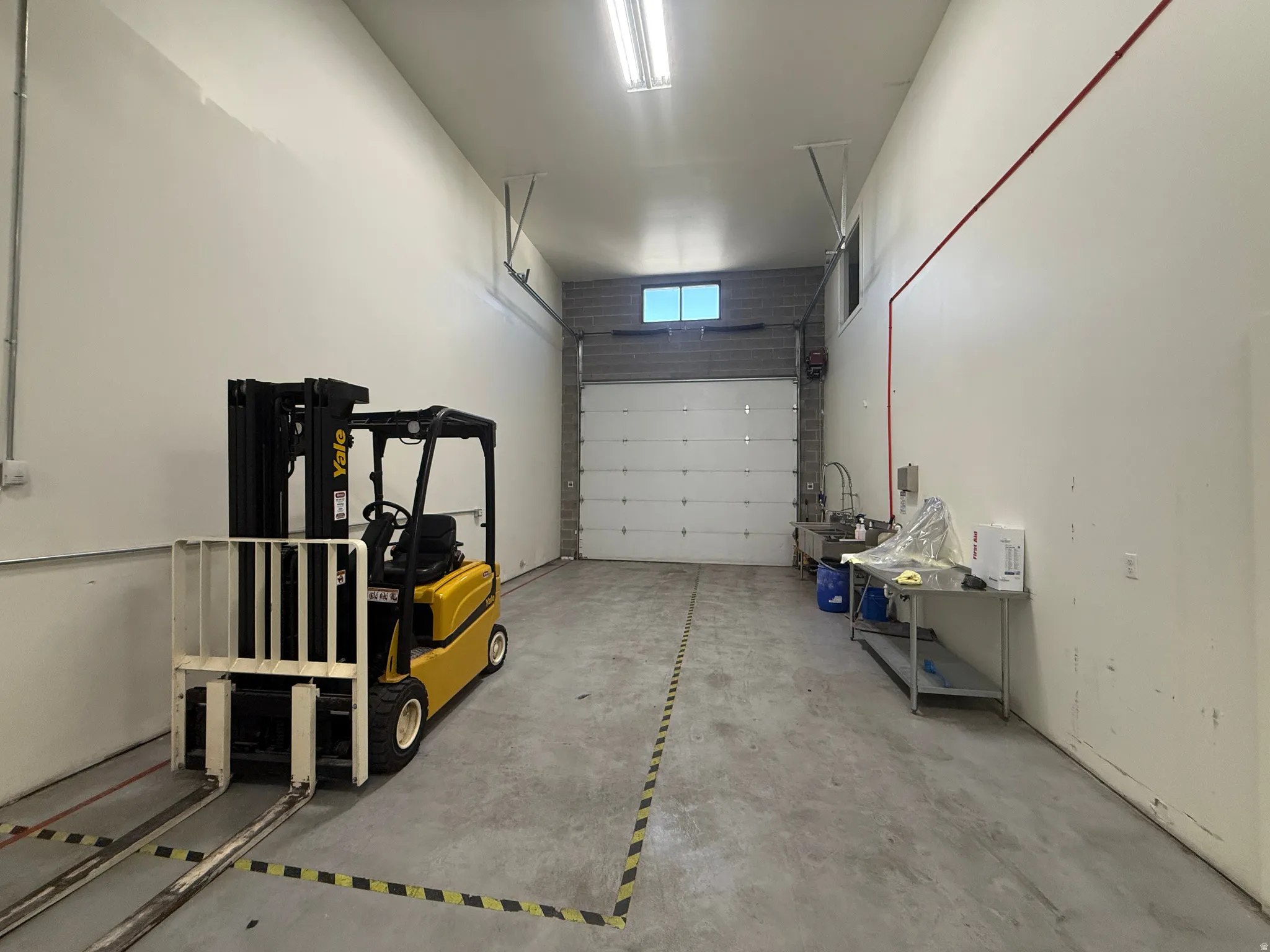 Concrete flooring with painted walls, overhead fluorescent lighting, and a roll-up door