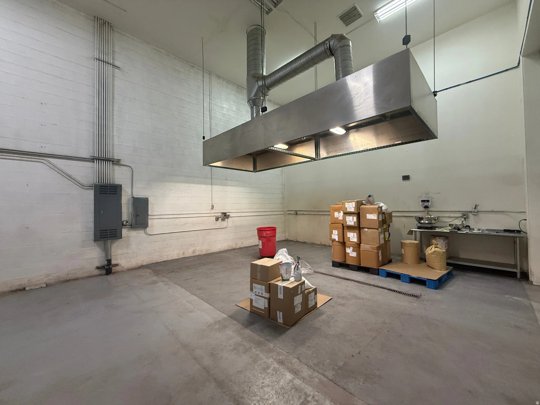 Industrial-style space featuring a commercial-grade stainless steel exhaust hood, exposed conduit, and a concrete floor