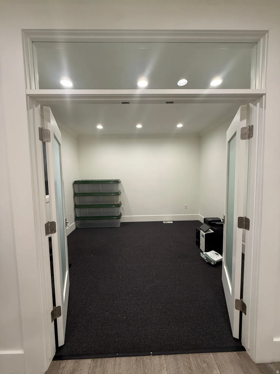 Double French doors with frosted glass panels, transom window, recessed lighting, and dark carpet flooring