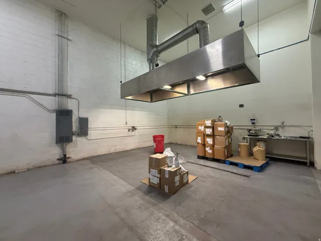 Industrial-style space featuring a commercial-grade stainless steel exhaust hood, exposed conduit, and a concrete floor