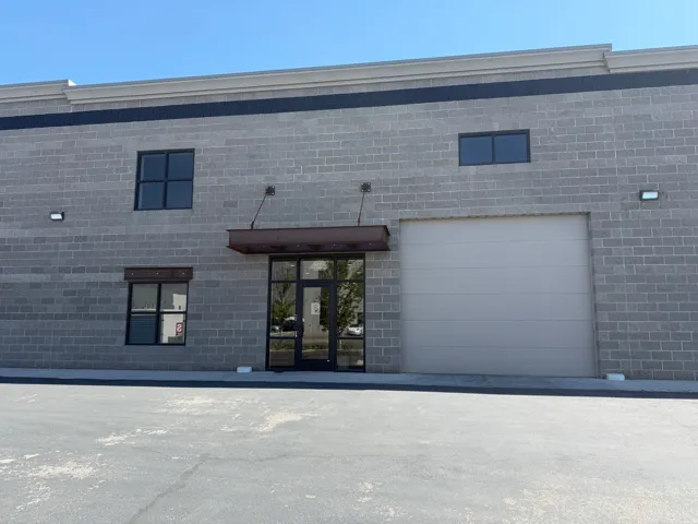Gray brick-finish exterior with a roll-up garage door, a glass entry door, and dark-framed windows