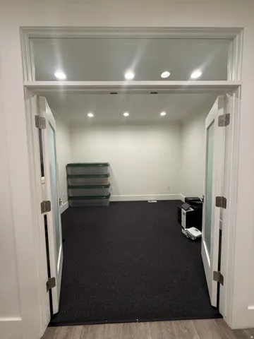 Double French doors with frosted glass panels, transom window, recessed lighting, and dark carpet flooring