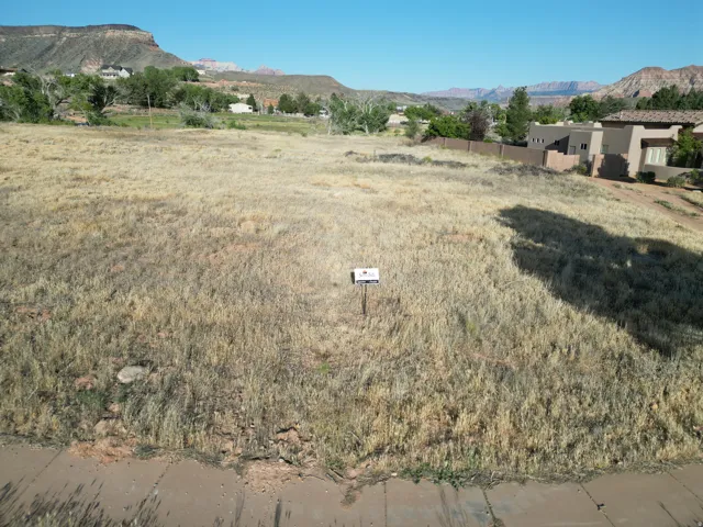 Expansive undeveloped lot featuring natural ground cover, a concrete curb, and distant mountain backdrops