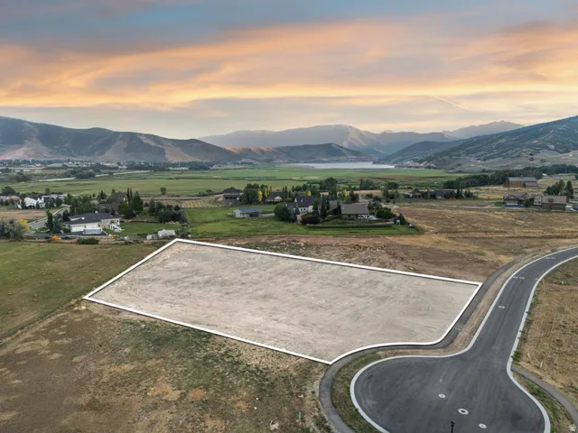Expansive lot featuring a paved road, mountain backdrop, and a distant lake