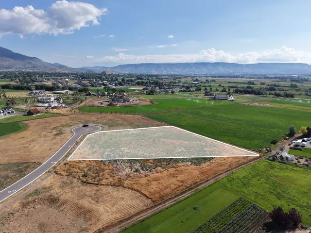 Expansive land parcel with surrounding agricultural fields, distant mountainous terrain, and an established paved road