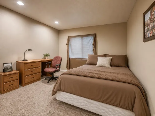 Recessed lighting, wood-finish desk with drawers, window with blinds, neutral-toned walls, and carpeted flooring