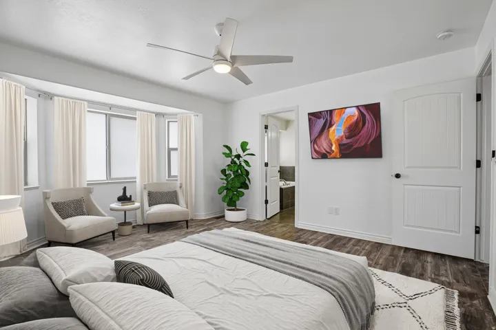 Wood-finish flooring, bay windows, ceiling fan with integrated lighting, and white paneled doors